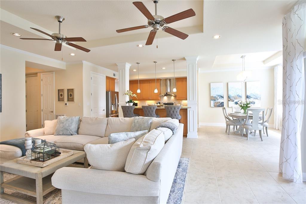 An open-concept living room and kitchen feature light tile flooring, ceiling fans, and neutral furniture — 7919 ST SIMONS STREET, UNIVERSITY PARK, FL