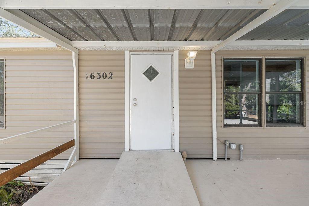 A beige house exterior features a white front door, a concrete ramp, and metal roofing — 16302 SE 57TH STREET, OCKLAWAHA, FL