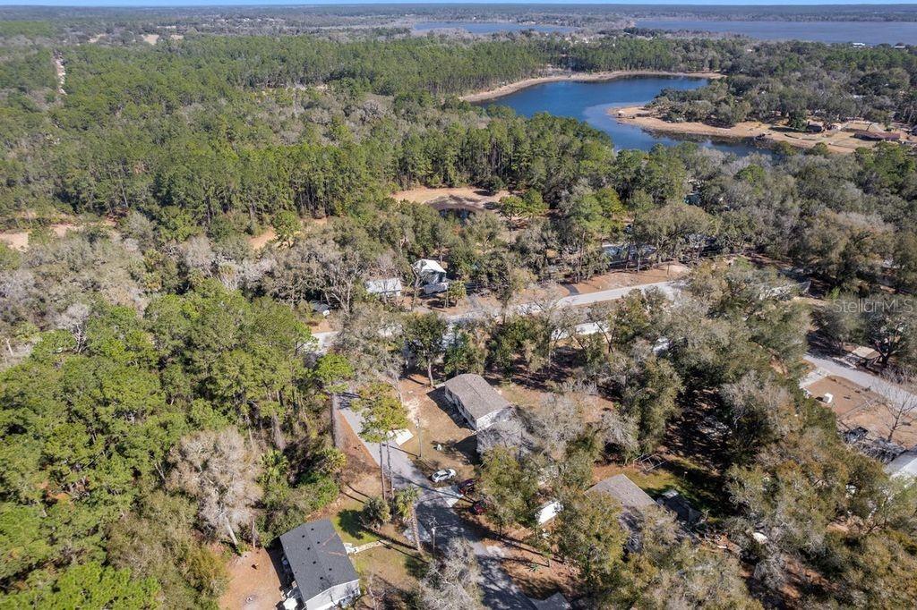 An aerial view shows several houses nestled among dense trees near a lake — 16302 SE 57TH STREET, OCKLAWAHA, FL