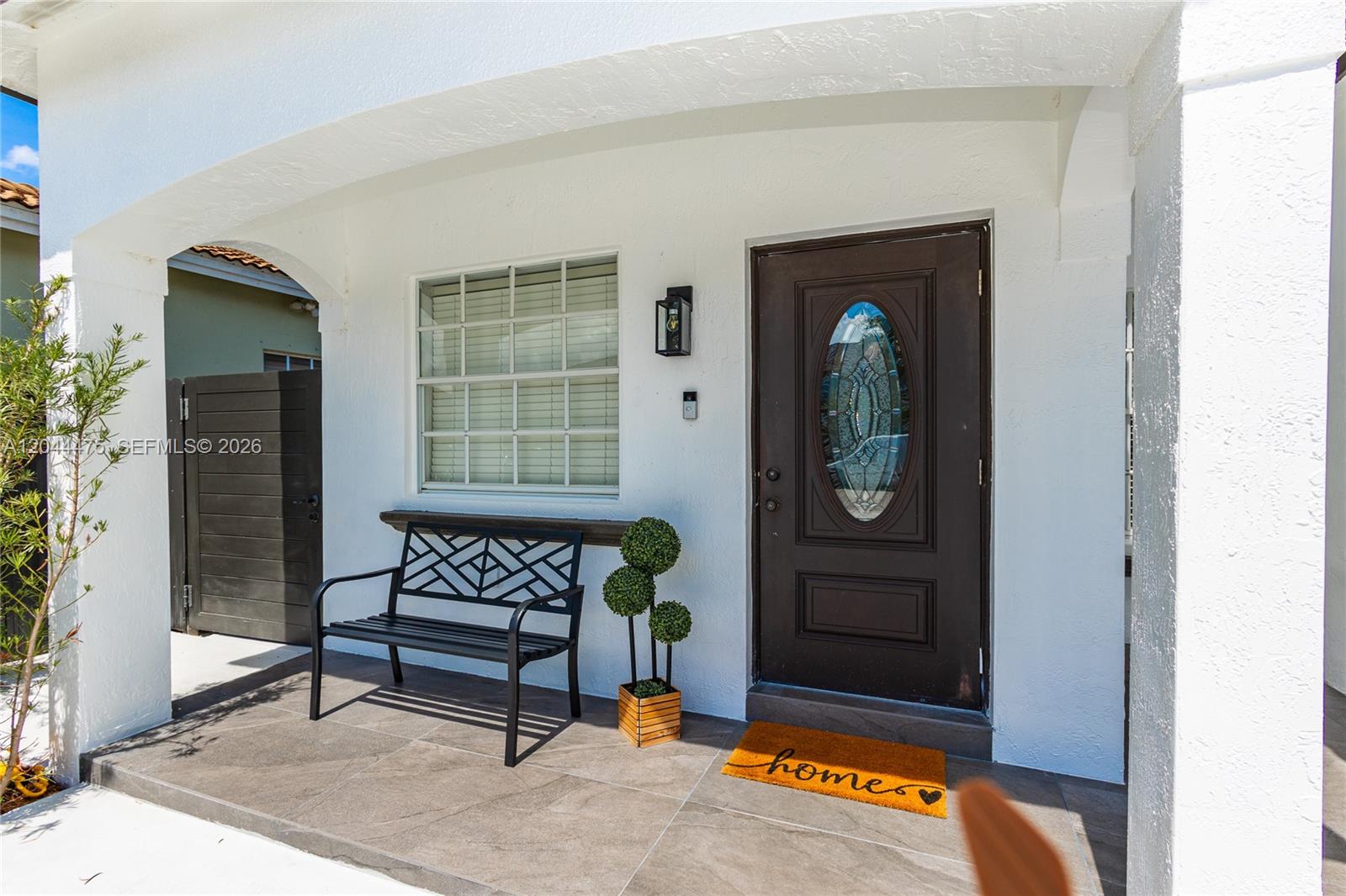 A covered front porch features a dark metal bench, a potted topiary, and a front door — 6939 SW 158th Ave, Miami FL 33193, MIAMI, FL