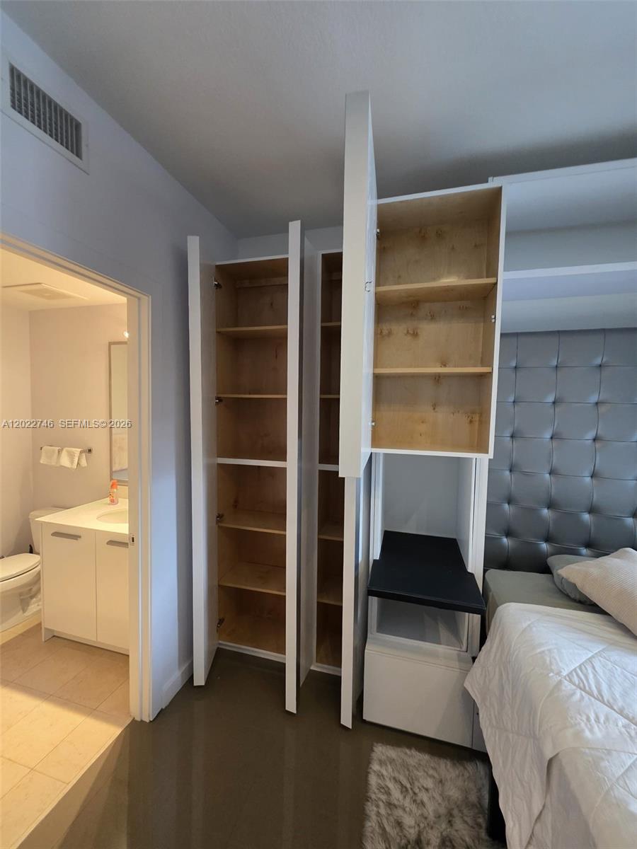 A bedroom features open white storage cabinets, a tufted headboard, and an adjacent bathroom — 1060 Brickell Ave # 2201, Miami FL 33131, MIAMI, FL
