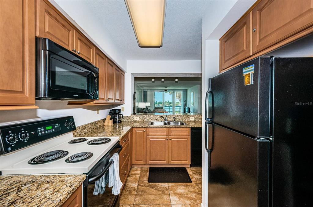 A kitchen with wood cabinets, granite countertops, black appliances, and a view of the water — 5801 BAHIA DEL MAR CIRCLE UNIT 512, ST PETERSBURG, FL