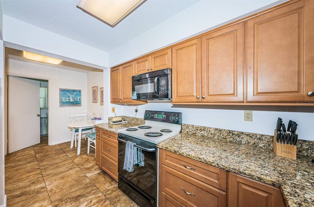 A kitchen with wood cabinets, granite countertops, a black stove, and tile flooring — 5801 BAHIA DEL MAR CIRCLE UNIT 512, ST PETERSBURG, FL