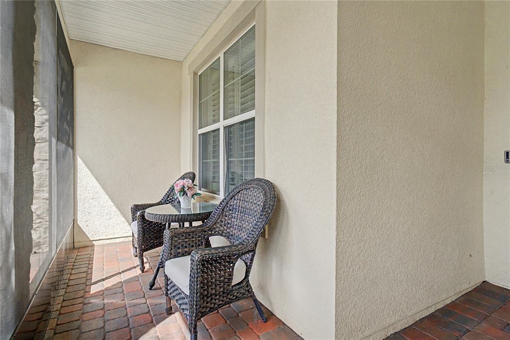 A covered patio features a brick floor, two wicker chairs, and a small glass table — 3051 AGOSTINO TERRACE, KISSIMMEE, FL
