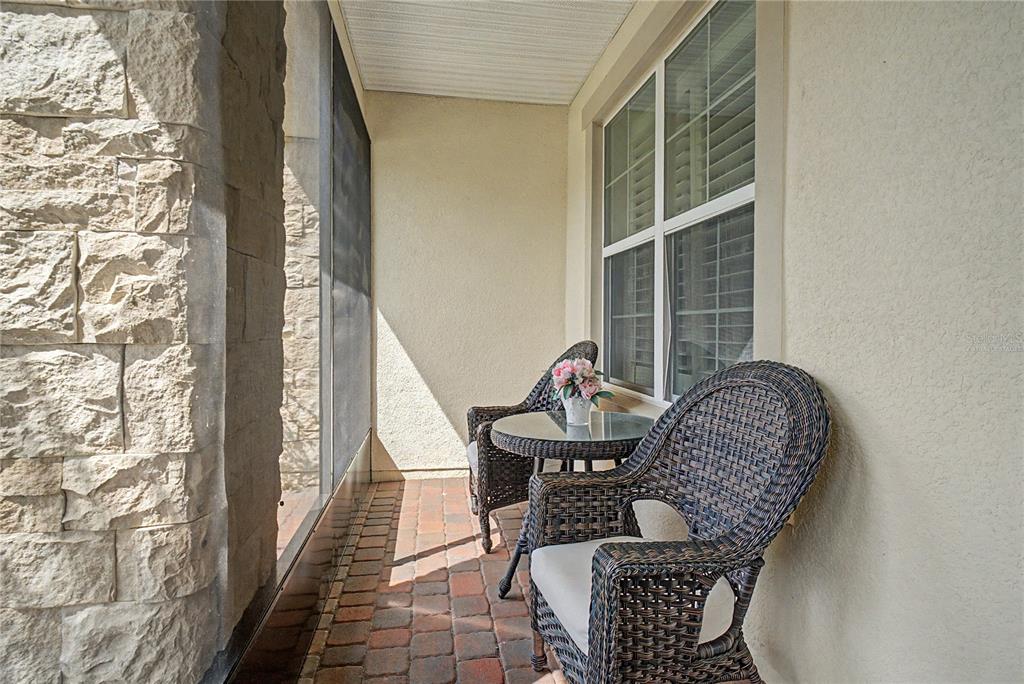 A screened-in patio features a brick floor, stone pillar, and two wicker chairs with a table — 3051 AGOSTINO TERRACE, KISSIMMEE, FL