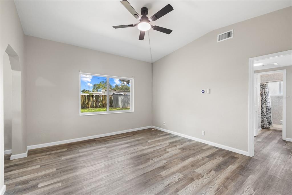 A bedroom with light gray walls, wood-look flooring, a ceiling fan, and an attached bathroom — 8616 SHIRLEY DRIVE, TEMPLE TERRACE, FL