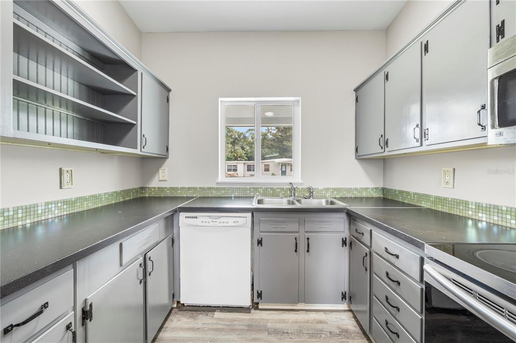 A kitchen features gray cabinets, black countertops, a green tiled backsplash, and a white dishwasher — 8616 SHIRLEY DRIVE, TEMPLE TERRACE, FL