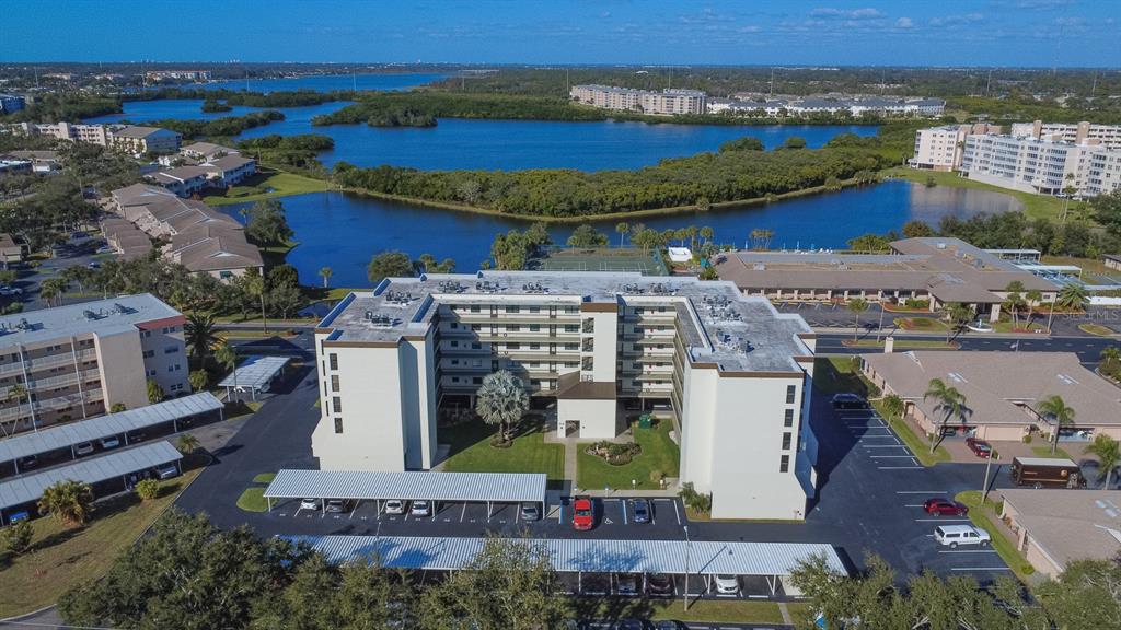 An aerial view of a multi-story apartment building with covered parking and a nearby lake — 9860 62ND TERRACE N UNIT 1014, ST PETERSBURG, FL