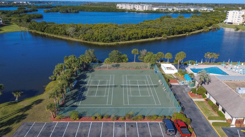 An aerial view shows two tennis courts next to a swimming pool and a lake — 9860 62ND TERRACE N UNIT 1014, ST PETERSBURG, FL