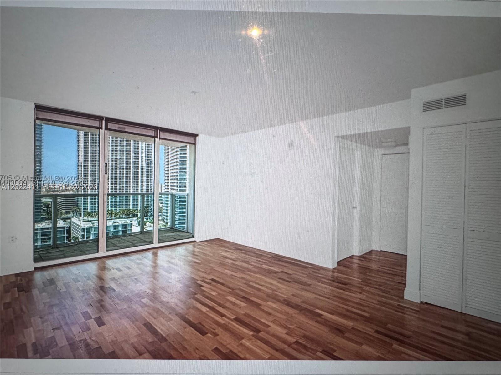 An empty room features hardwood floors, white walls, and floor-to-ceiling windows overlooking city buildings — 31 SE 5th St # 2507, Miami FL 33131, MIAMI, FL
