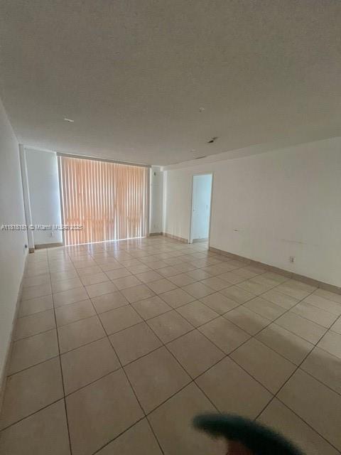 An empty living room with light-colored tile flooring and vertical blinds covering a large window — 13499 Biscayne Blvd # 602, North Miami FL 33181, NORTH MIAMI, FL