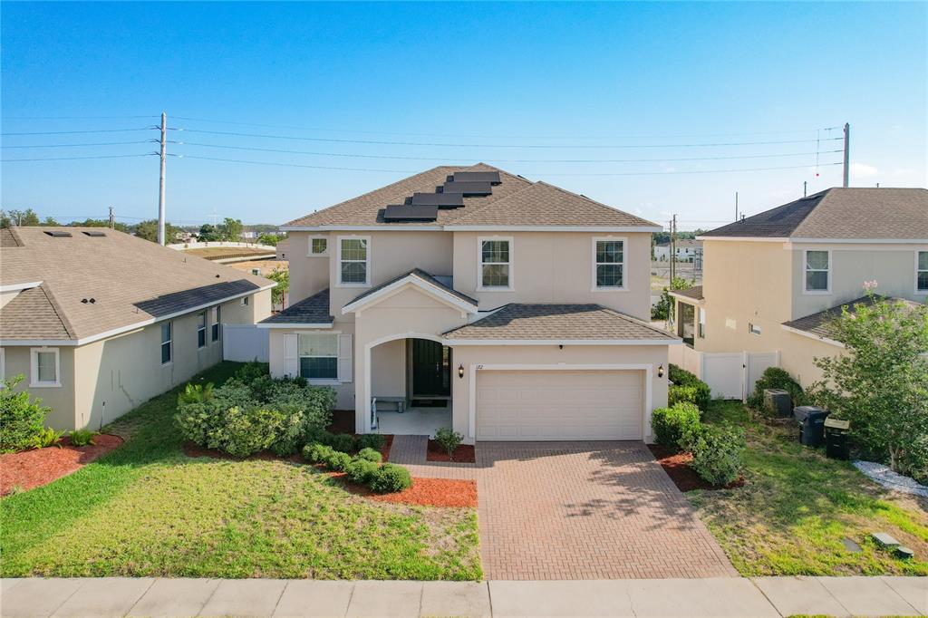A two-story suburban house with a brick driveway, a two-car garage, and rooftop solar panels — 172 SEVILLE DRIVE, DAVENPORT, FL