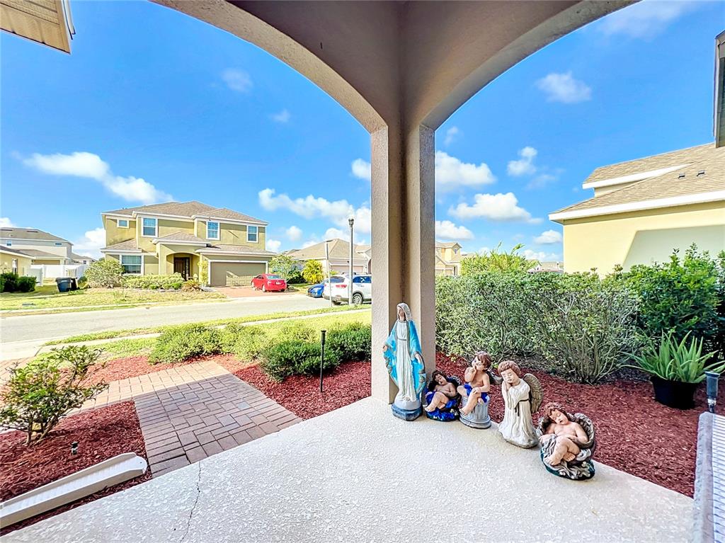 A covered porch features a concrete floor, a brick walkway, and several religious statues — 172 SEVILLE DRIVE, DAVENPORT, FL