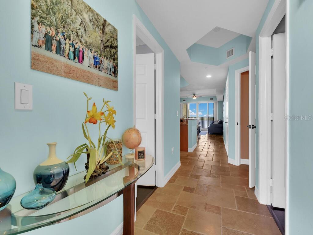 A hallway with light blue walls and tile flooring leads toward an open living area — 2797 1ST STREET UNIT 1605, FORT MYERS, FL