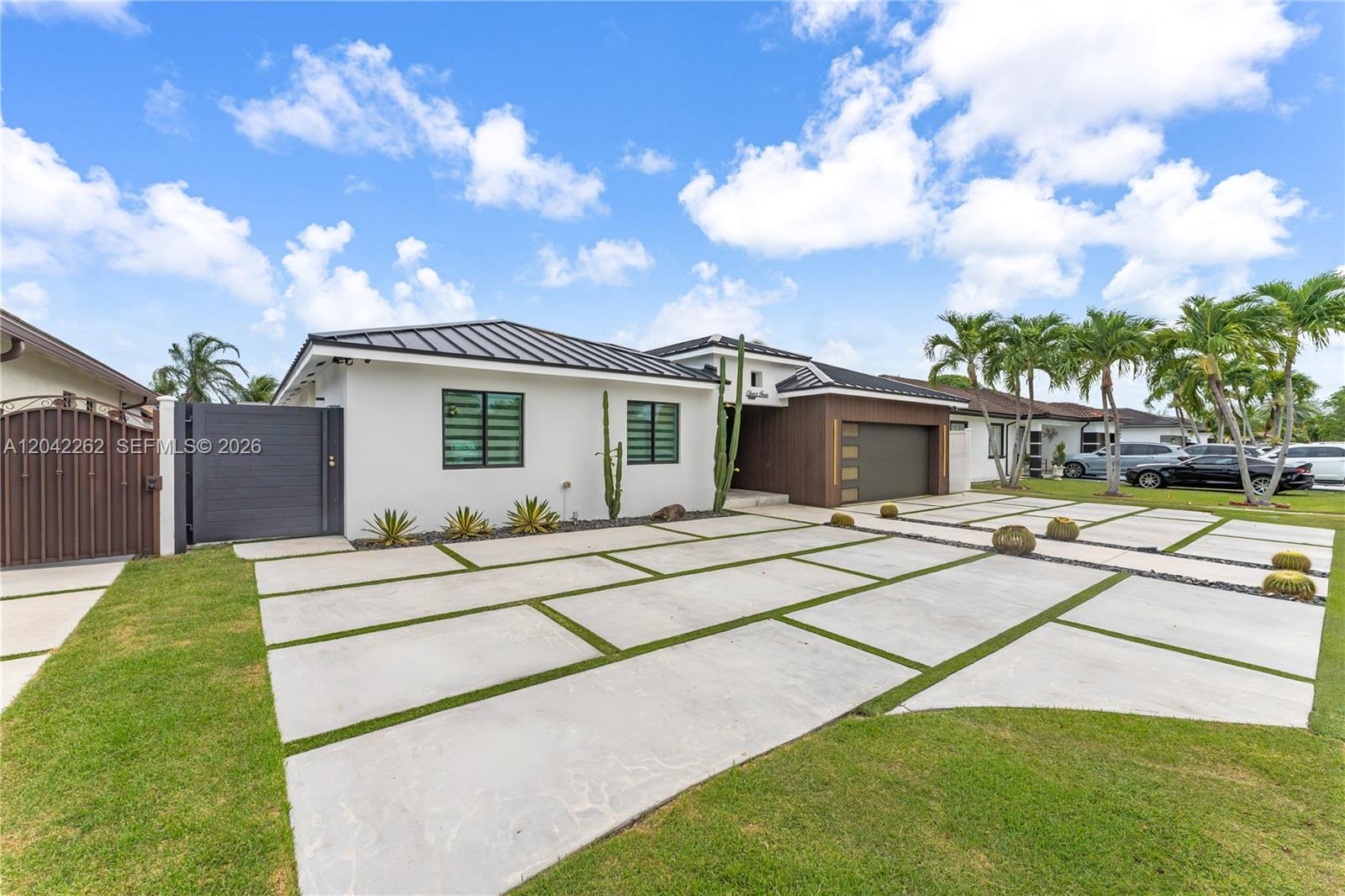 A modern single-story house features a white exterior, dark metal roof, and a grid-patterned driveway — 12772 SW 209th St, Miami FL 33177, MIAMI, FL