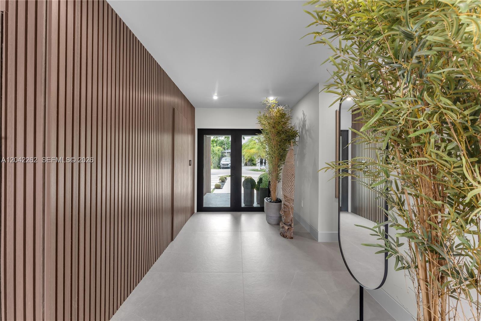 A modern entryway features a slatted wood wall, large-format tile flooring, and a glass door — 12772 SW 209th St, Miami FL 33177, MIAMI, FL