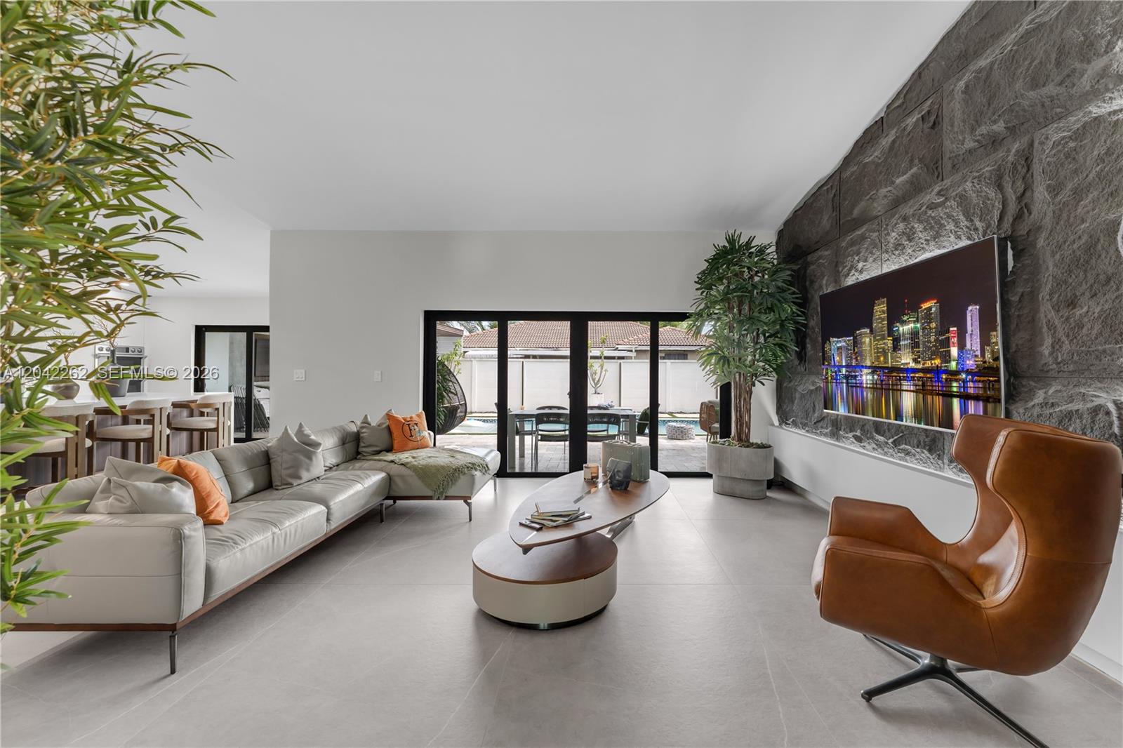 A modern living room features a stone accent wall, leather armchair, and large sliding glass doors — 12772 SW 209th St, Miami FL 33177, MIAMI, FL