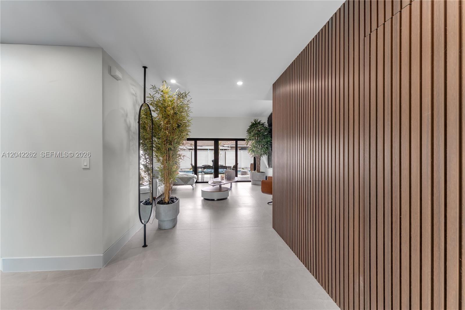 A hallway with a wood-slat wall leads to a living area with large glass doors — 12772 SW 209th St, Miami FL 33177, MIAMI, FL