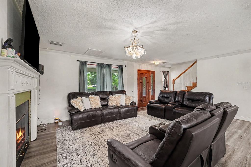 A living room features a fireplace, dark leather sofas, a chandelier, and a wooden staircase — 5710 BARNA AVENUE, TITUSVILLE, FL
