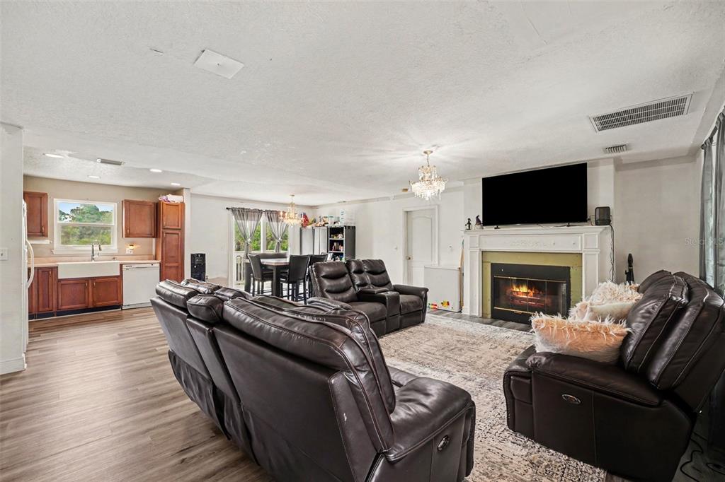An open-concept living room features a fireplace, dark leather furniture, and an adjacent kitchen area — 5710 BARNA AVENUE, TITUSVILLE, FL