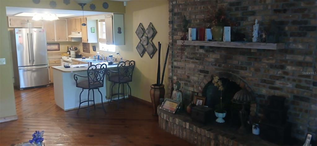 A kitchen with a breakfast bar and stainless steel refrigerator sits beside a brick fireplace — 855 N RIDGEWOOD AVENUE, ORMOND BEACH, FL