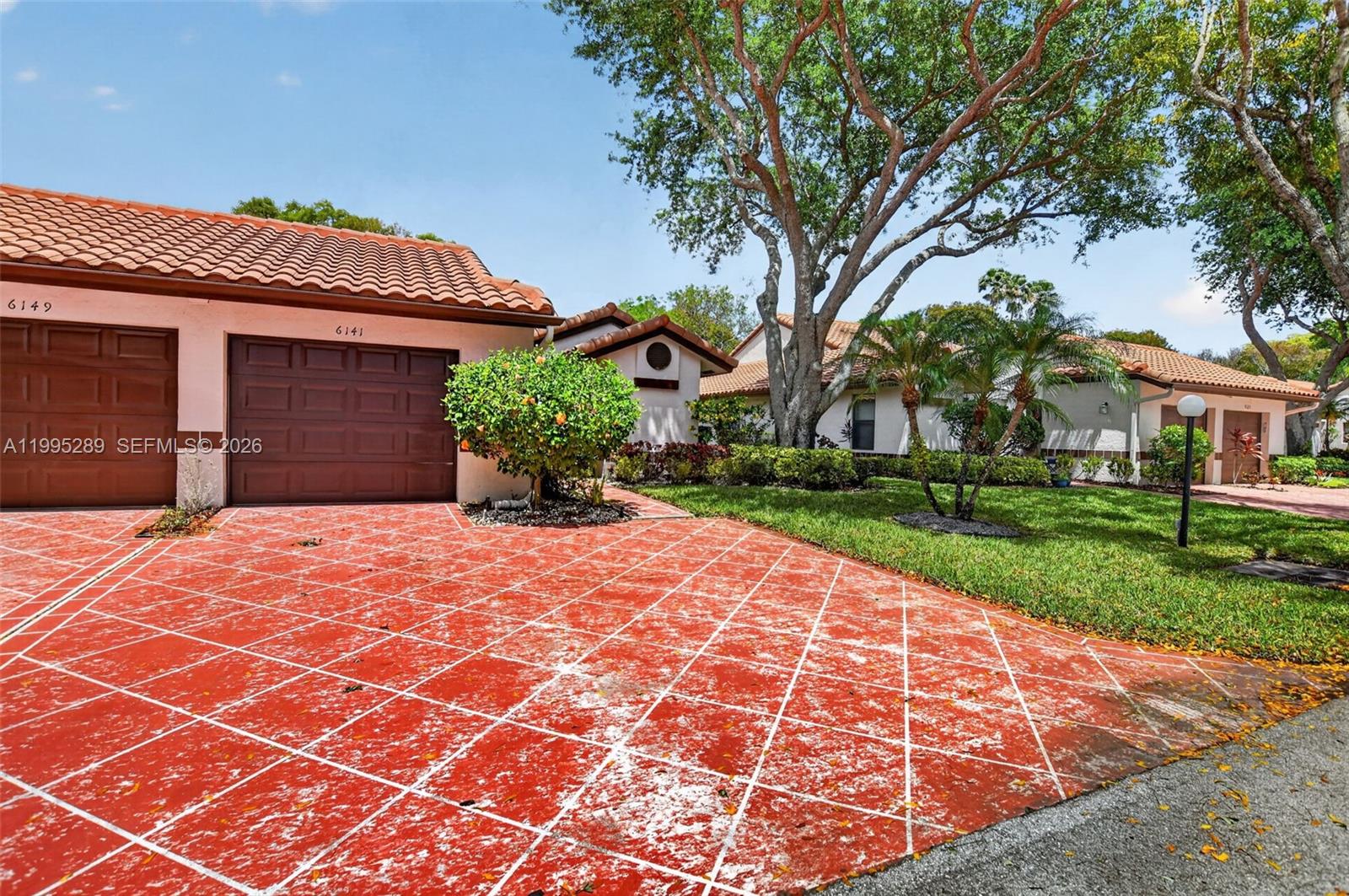 A house exterior features a red patterned driveway, a two-car garage, and mature trees — 6141 SE Sunny Pointe Cir, Delray Beach FL 33484, DELRAY BEACH, FL