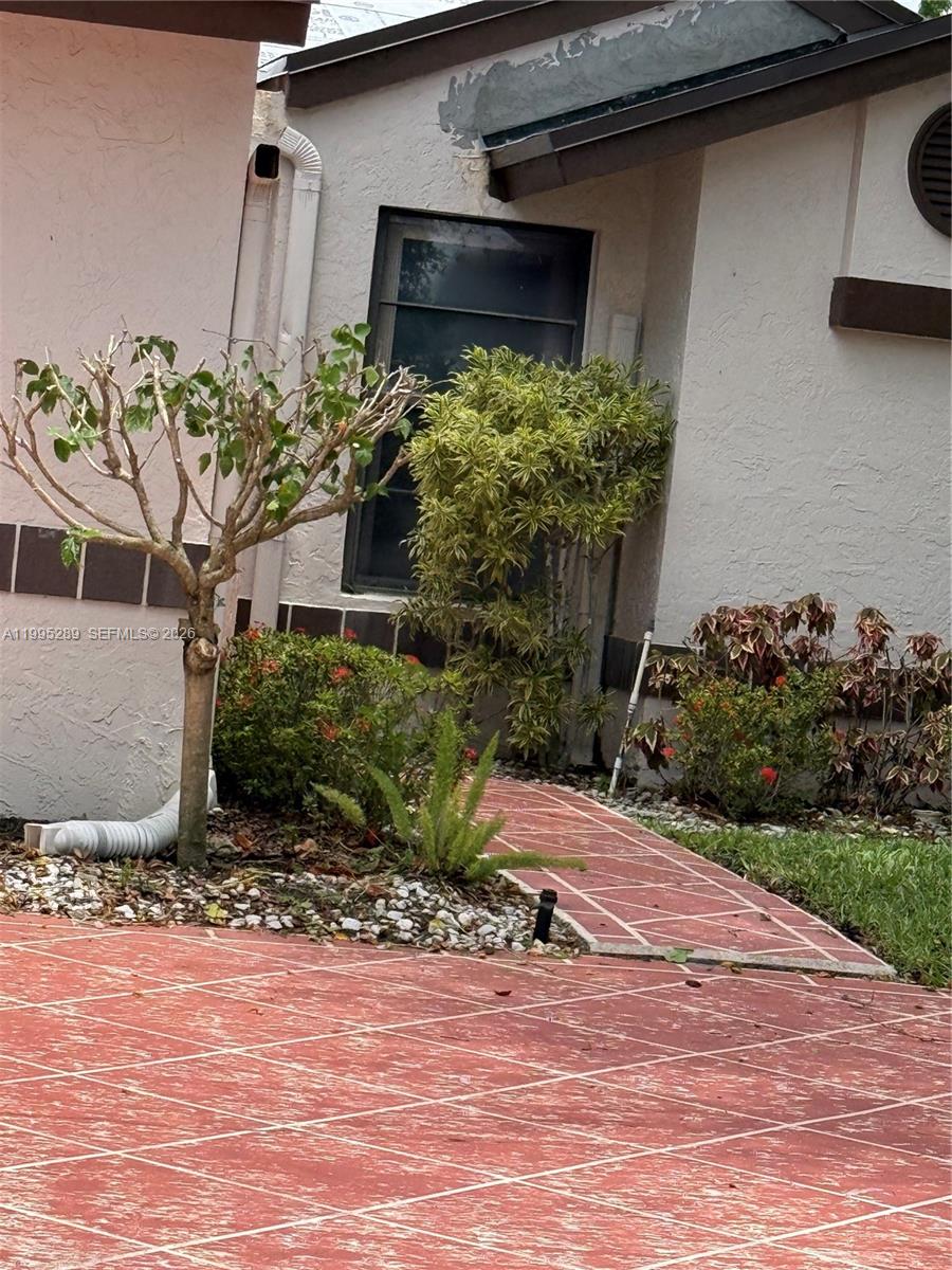 A paved walkway leads to the entrance of a house with stucco walls and landscaping — 6141 SE Sunny Pointe Cir, Delray Beach FL 33484, DELRAY BEACH, FL