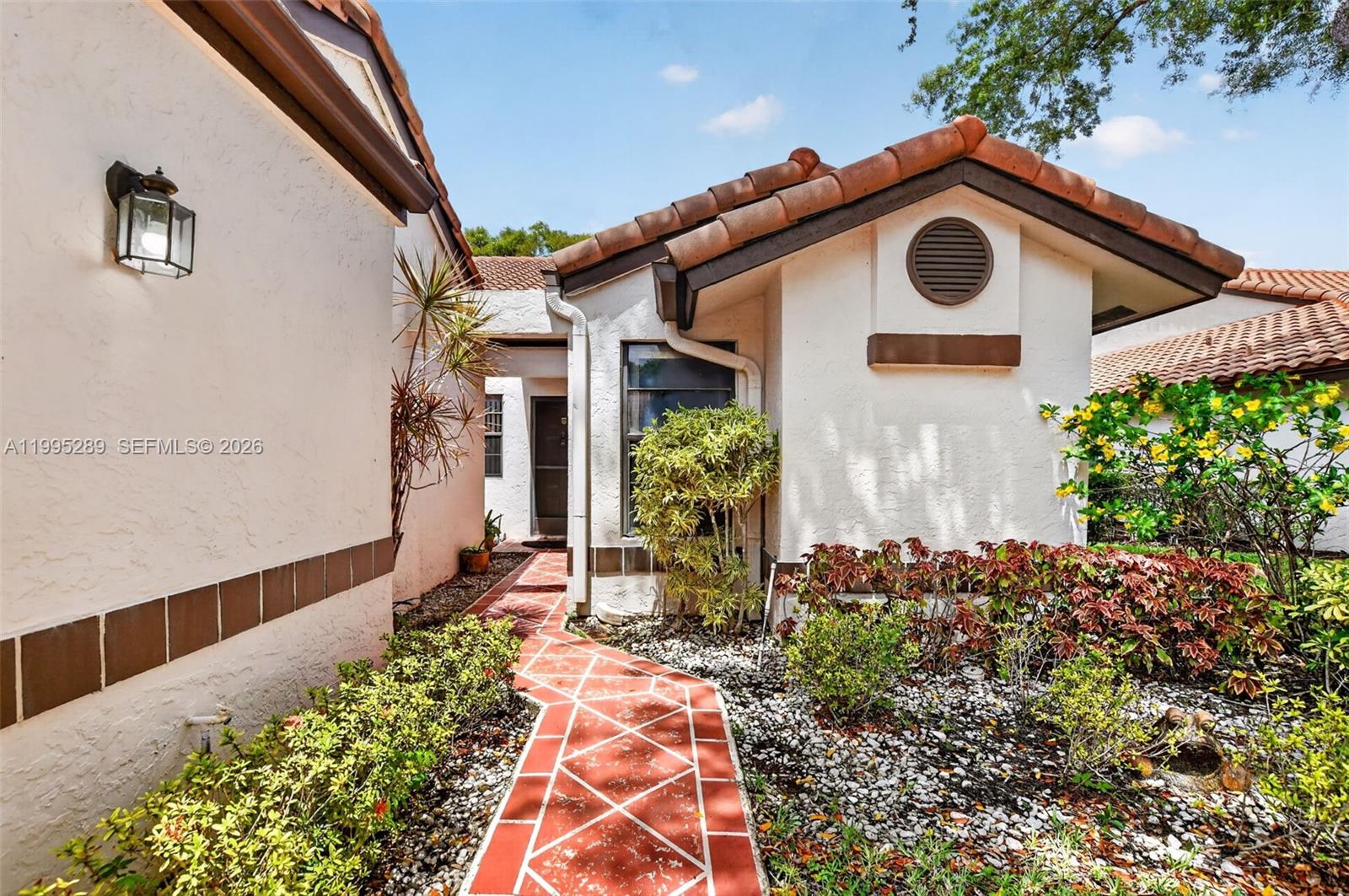 A red-tiled walkway leads to the entrance of a stucco home with a tiled roof — 6141 SE Sunny Pointe Cir, Delray Beach FL 33484, DELRAY BEACH, FL