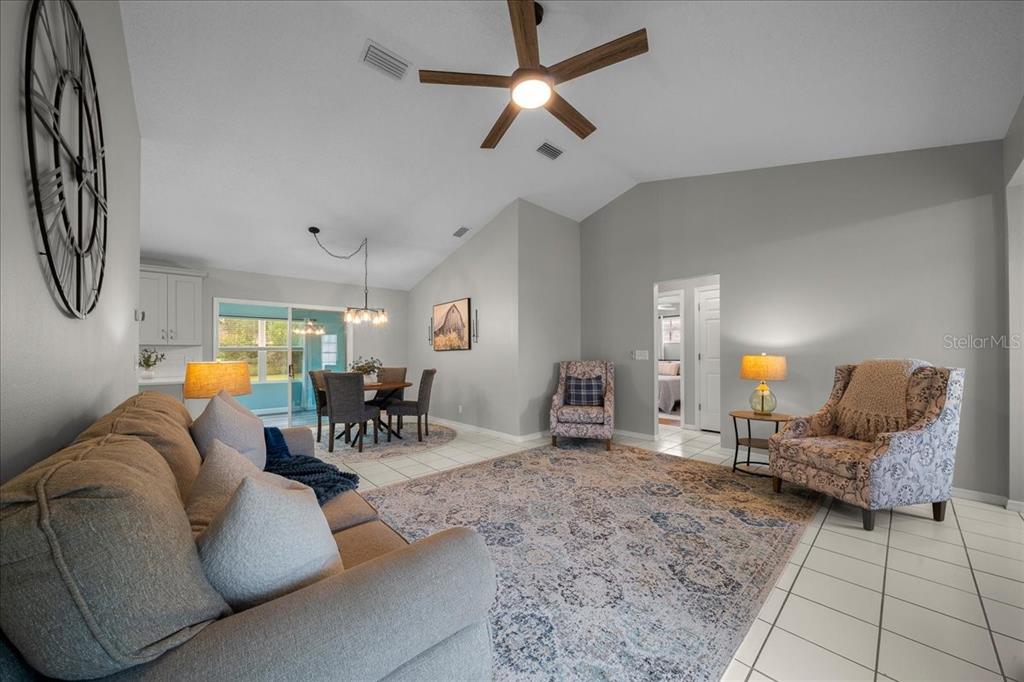 A living room with a vaulted ceiling, ceiling fan, tile flooring, and an adjacent dining area — 4504 NW 32ND STREET, OCALA, FL