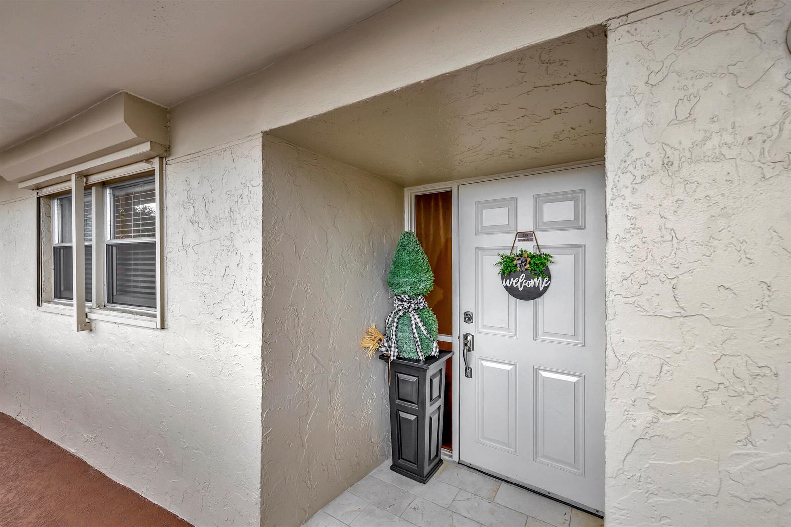 A white front door with a welcome sign sits beside a decorative topiary on a porch — 1537 E Hillsboro Boulevard # 239, Deerfield Beach FL 33441, DEERFIELD BEACH, FL