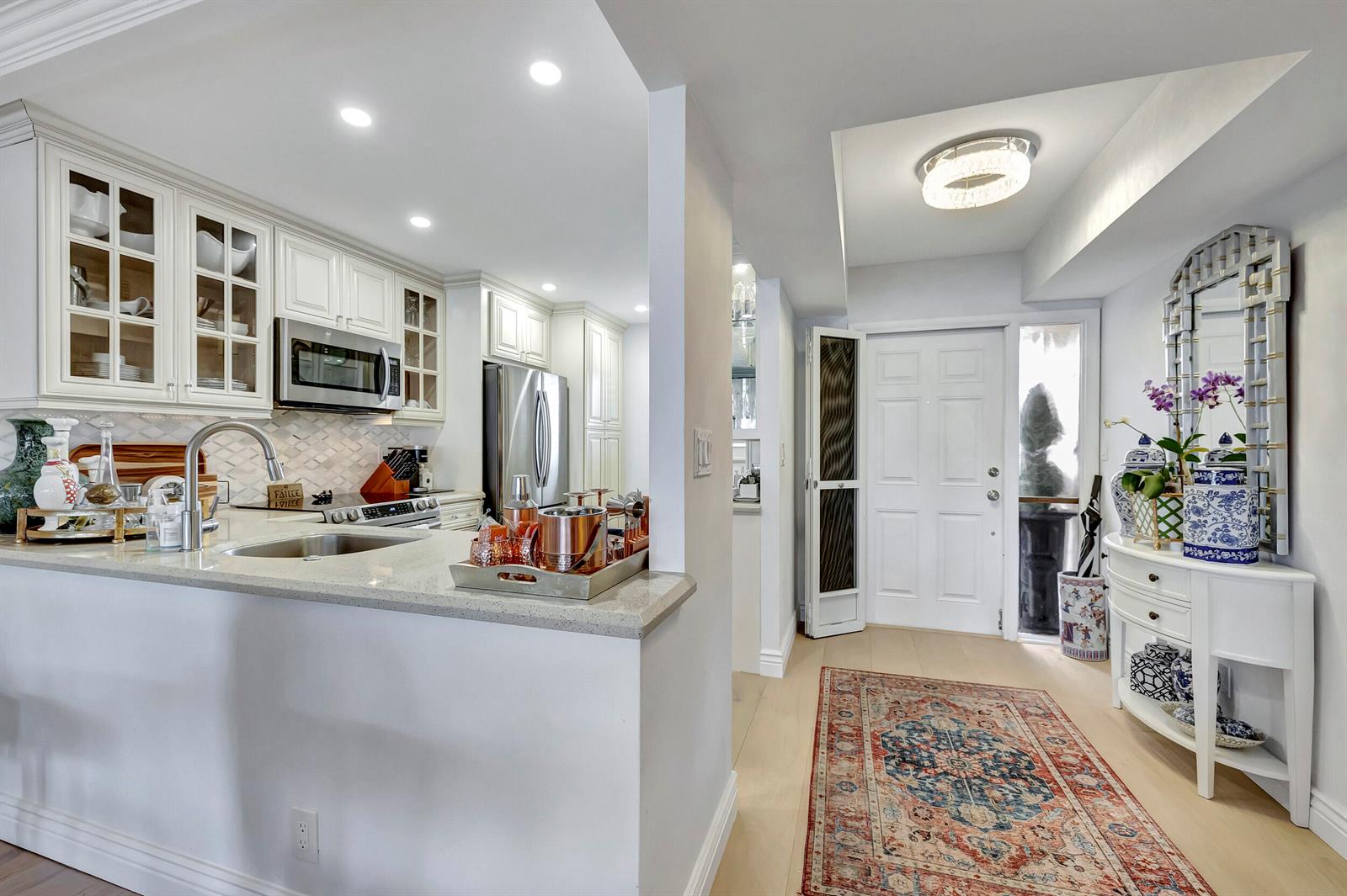 A kitchen with white cabinets and a quartz countertop opens to an entryway with a rug — 1537 E Hillsboro Boulevard # 239, Deerfield Beach FL 33441, DEERFIELD BEACH, FL