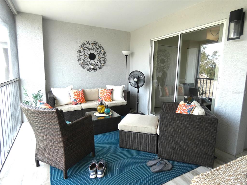 A covered balcony features wicker patio furniture, a blue area rug, and a sliding glass door — 4639 CHAPEL HILL DRIVE UNIT 2924, SARASOTA, FL