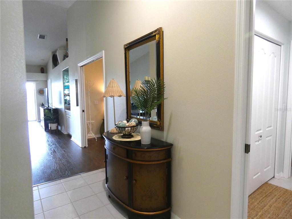 A hallway with tile flooring features a decorative console table, mirror, and lamp — 4639 CHAPEL HILL DRIVE UNIT 2924, SARASOTA, FL