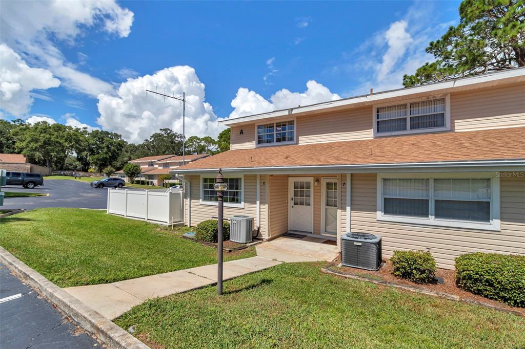 A two-story tan vinyl-sided townhouse with a brown shingled roof and a concrete walkway — 11001 SE SUNSET HARBOR RD UNIT A08, SUMMERFIELD, FL