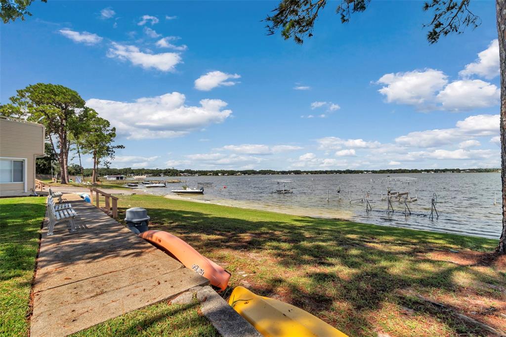 A wooden walkway leads along a grassy shoreline toward a lake with several boat docks — 11001 SE SUNSET HARBOR RD UNIT A08, SUMMERFIELD, FL