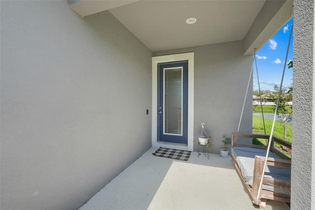 A covered porch features a blue front door, a hanging bench, and a concrete floor — 4347 SILVER CREEK STREET, KISSIMMEE, FL