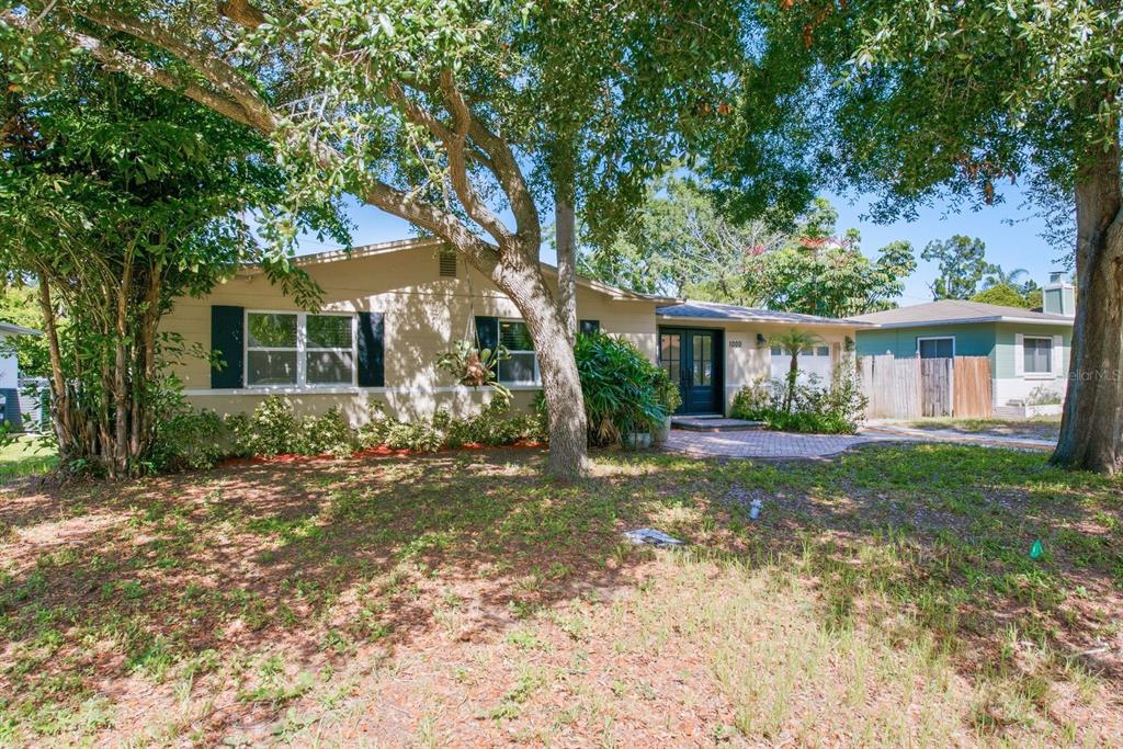 A single-story house with a tan exterior, dark shutters, and a brick walkway under trees — 1000 S EVERGREEN AVENUE, CLEARWATER, FL