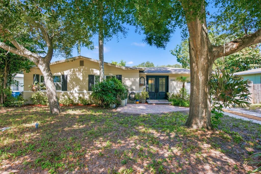A single-story house with a beige exterior, dark double front doors, and large shade trees — 1000 S EVERGREEN AVENUE, CLEARWATER, FL