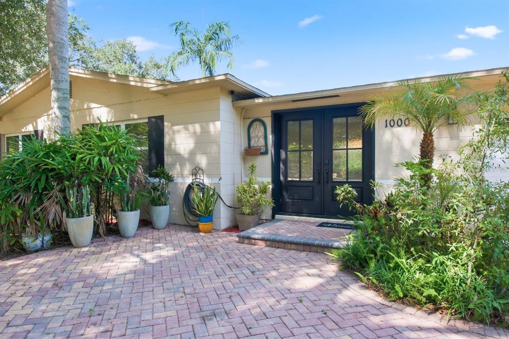 A house exterior features a brick paver driveway, double glass doors, and lush potted plants — 1000 S EVERGREEN AVENUE, CLEARWATER, FL