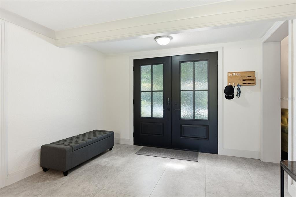 An entryway features a gray tufted bench, tile flooring, and black double front doors — 1000 S EVERGREEN AVENUE, CLEARWATER, FL