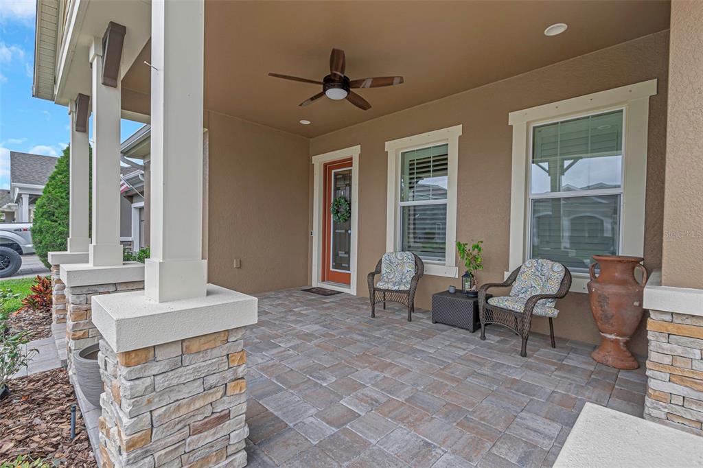 A covered front porch features stone-based columns, a ceiling fan, and two wicker chairs — 4239 WOODLAND RETREAT BOULEVARD, NEW PORT RICHEY, FL