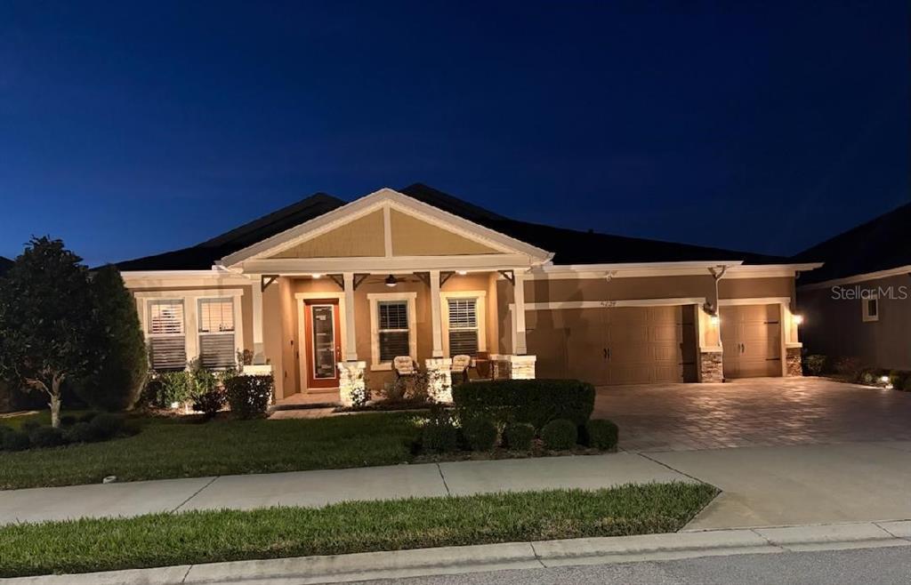 A single-story house with a front porch, stone accents, and a three-car garage at dusk — 4239 WOODLAND RETREAT BOULEVARD, NEW PORT RICHEY, FL