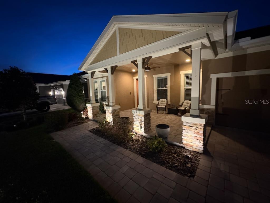 A paved walkway leads to a covered front porch with stone pillars and outdoor seating — 4239 WOODLAND RETREAT BOULEVARD, NEW PORT RICHEY, FL