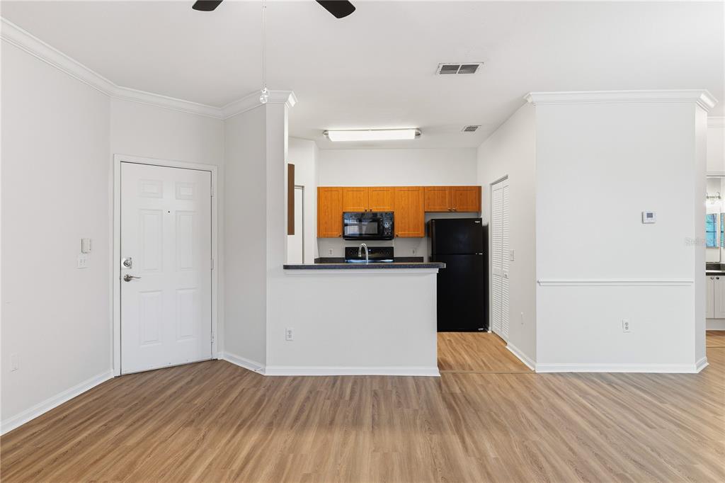 A kitchen with wood cabinets and black appliances overlooks a living area with wood flooring — 2171 PORTOFINO PLACE UNIT 7-2723, PALM HARBOR, FL