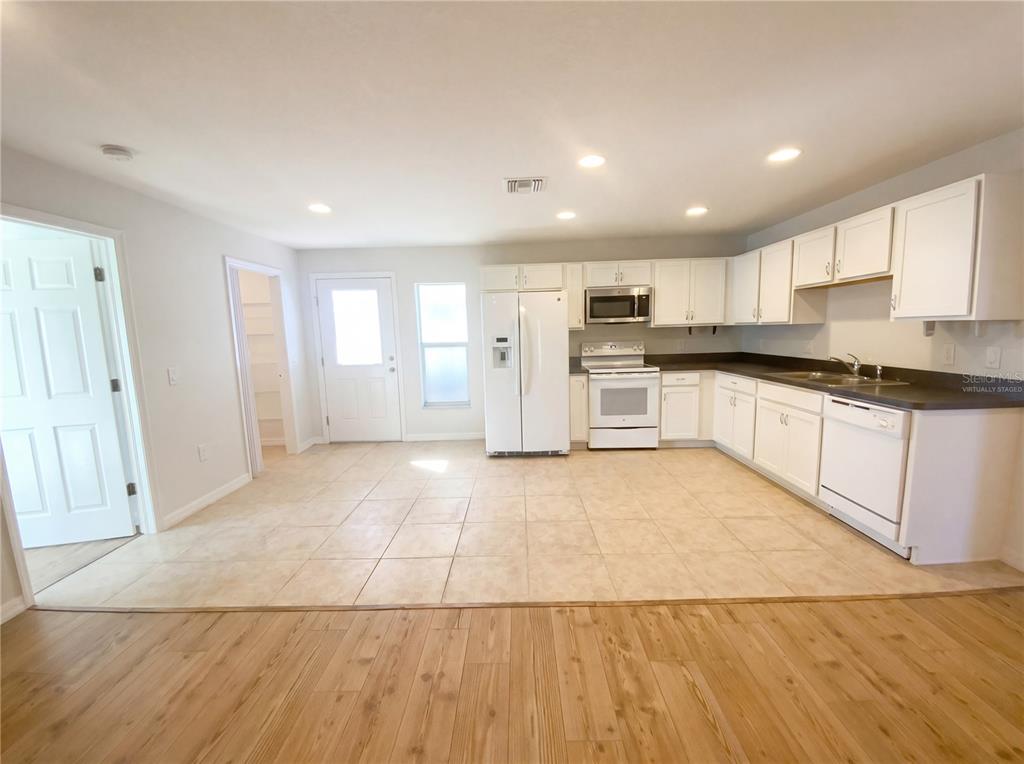 A kitchen with white cabinets, white appliances, and tile flooring adjacent to a wood-floored area — 11275 LINDEN DRIVE, SPRING HILL, FL