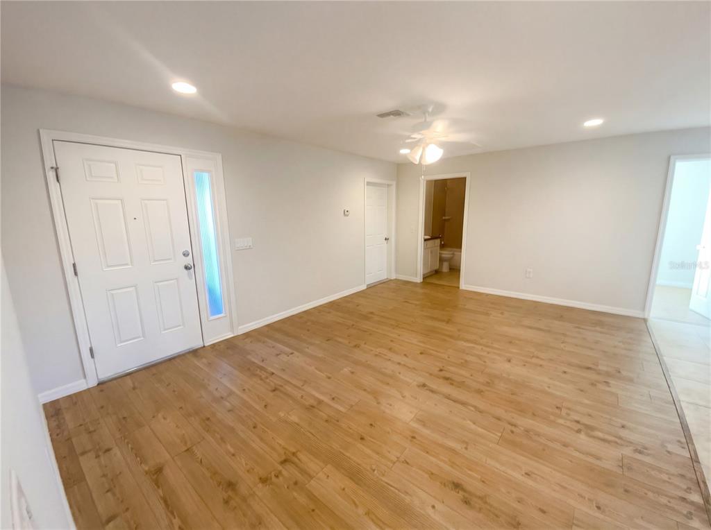 An interior view of a room with light wood-look flooring, a white front door, and recessed lighting — 11275 LINDEN DRIVE, SPRING HILL, FL