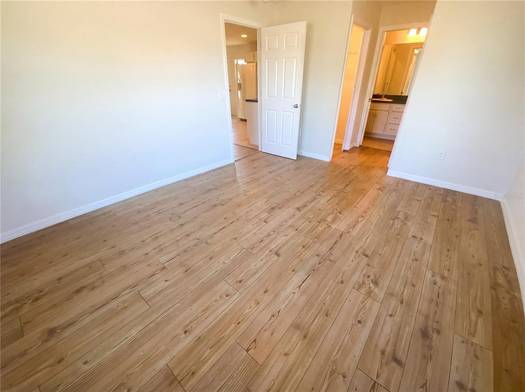 An empty room with light wood-look flooring, a white door, and an adjacent bathroom — 11275 LINDEN DRIVE, SPRING HILL, FL