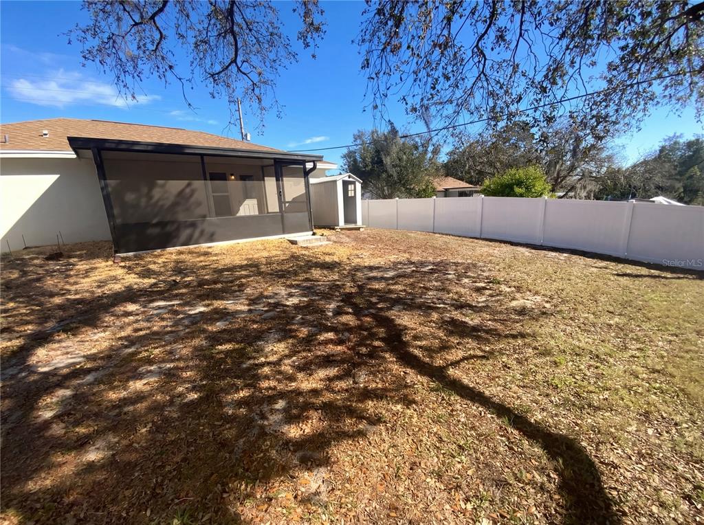 A backyard features a screened-in porch, a small storage shed, and a white vinyl fence — 11275 LINDEN DRIVE, SPRING HILL, FL
