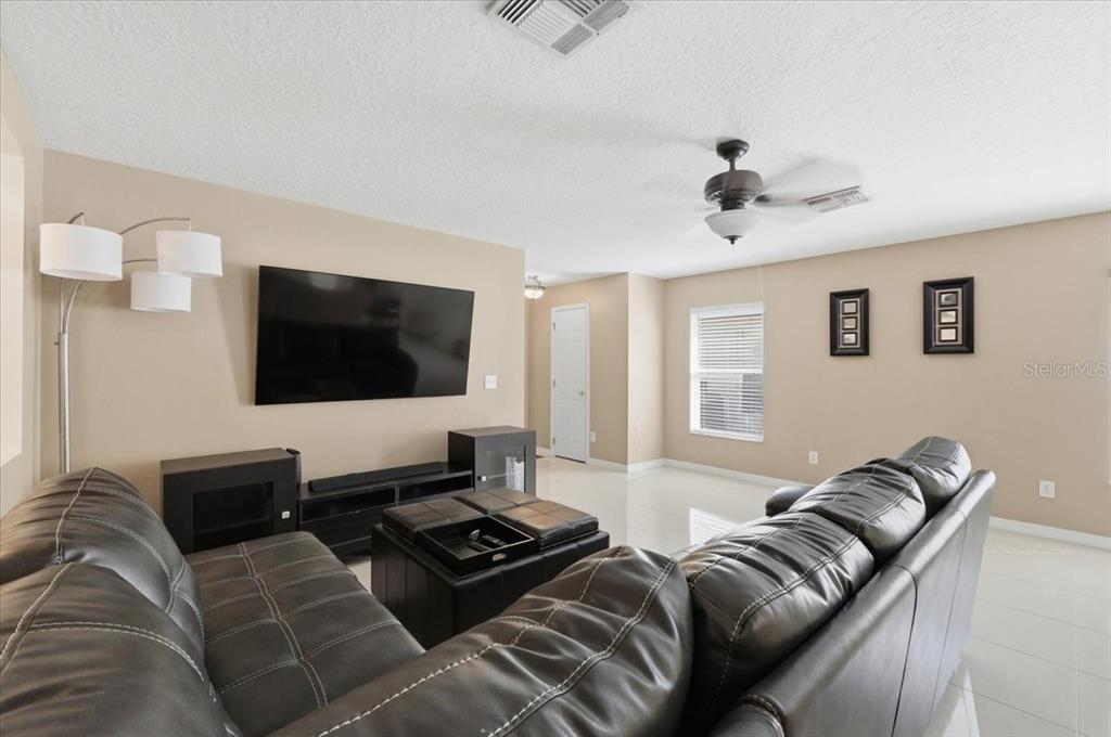 A living room features a dark leather sectional, a wall-mounted television, and tile flooring — 14852 PELLICER DRIVE, ORLANDO, FL