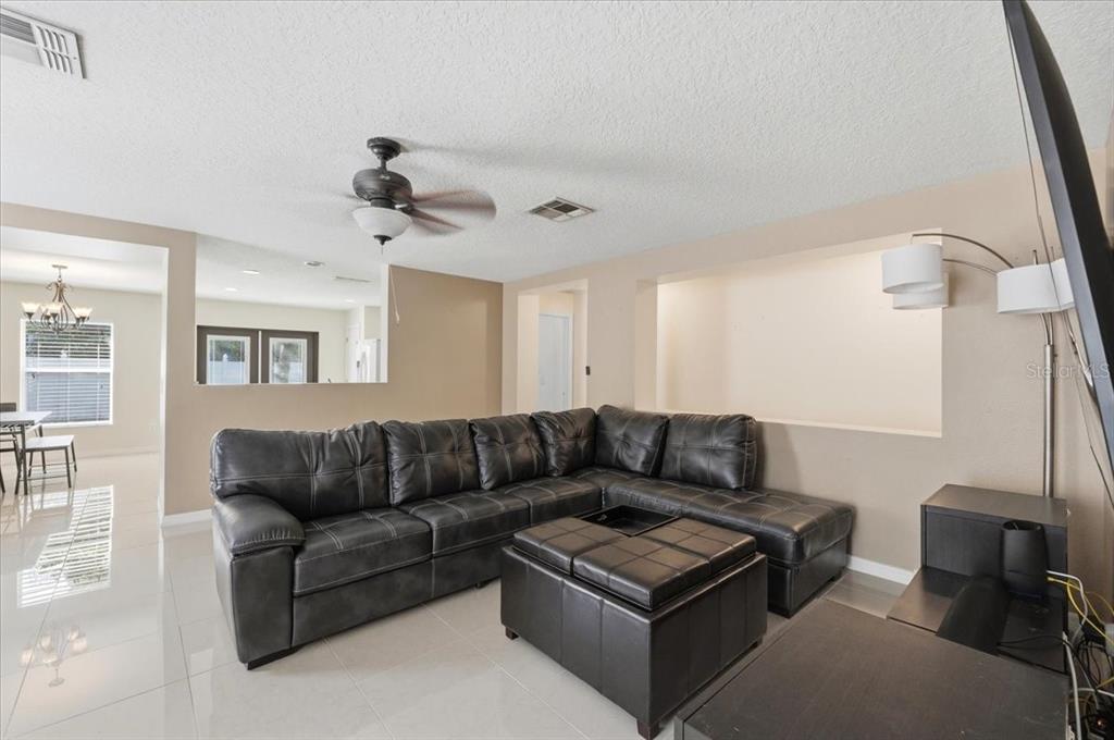 A living room features a large dark leather sectional, a matching ottoman, and tile flooring — 14852 PELLICER DRIVE, ORLANDO, FL